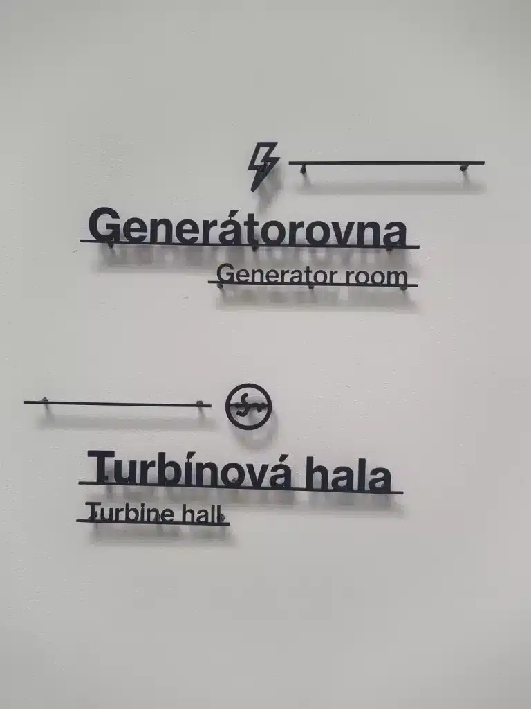 Directional signs in Czech and English inside EPO 01 contemporary art gallery, showing "Generátorovna" (Generator room) and "Turbínová hala" (Turbine hall).