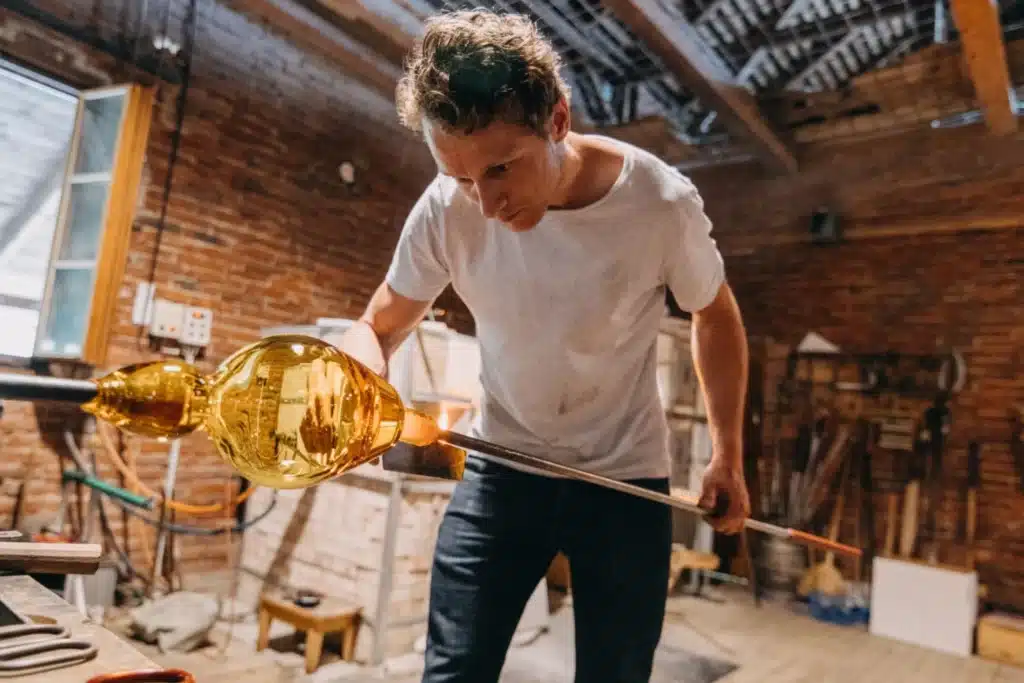 A glassmaker from Ajeto Glassworks shaping a molten glass piece during a public demonstration.