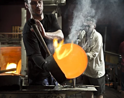Two craftsmen shaping molten glass at Ajeto Glassworks during a live demonstration.