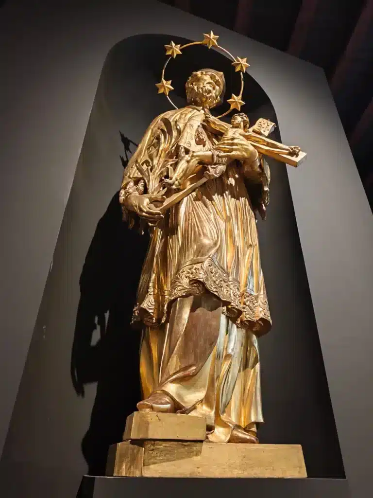 Golden statue of Saint John of Nepomuk displayed at the Flowing Through Czech Culture – The Vltava Exhibition in Prague, featured on SOLARIS Language School blog about Czech culture and learning Czech online.