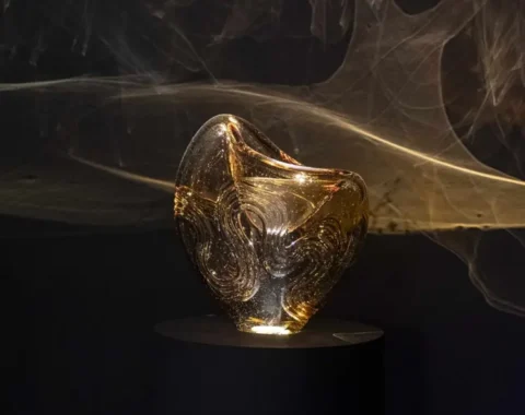 Glass sculpture titled 'Vltava' from the Flowing Through Czech Culture exhibition in Prague, illuminated amber artwork representing the Czech river.
